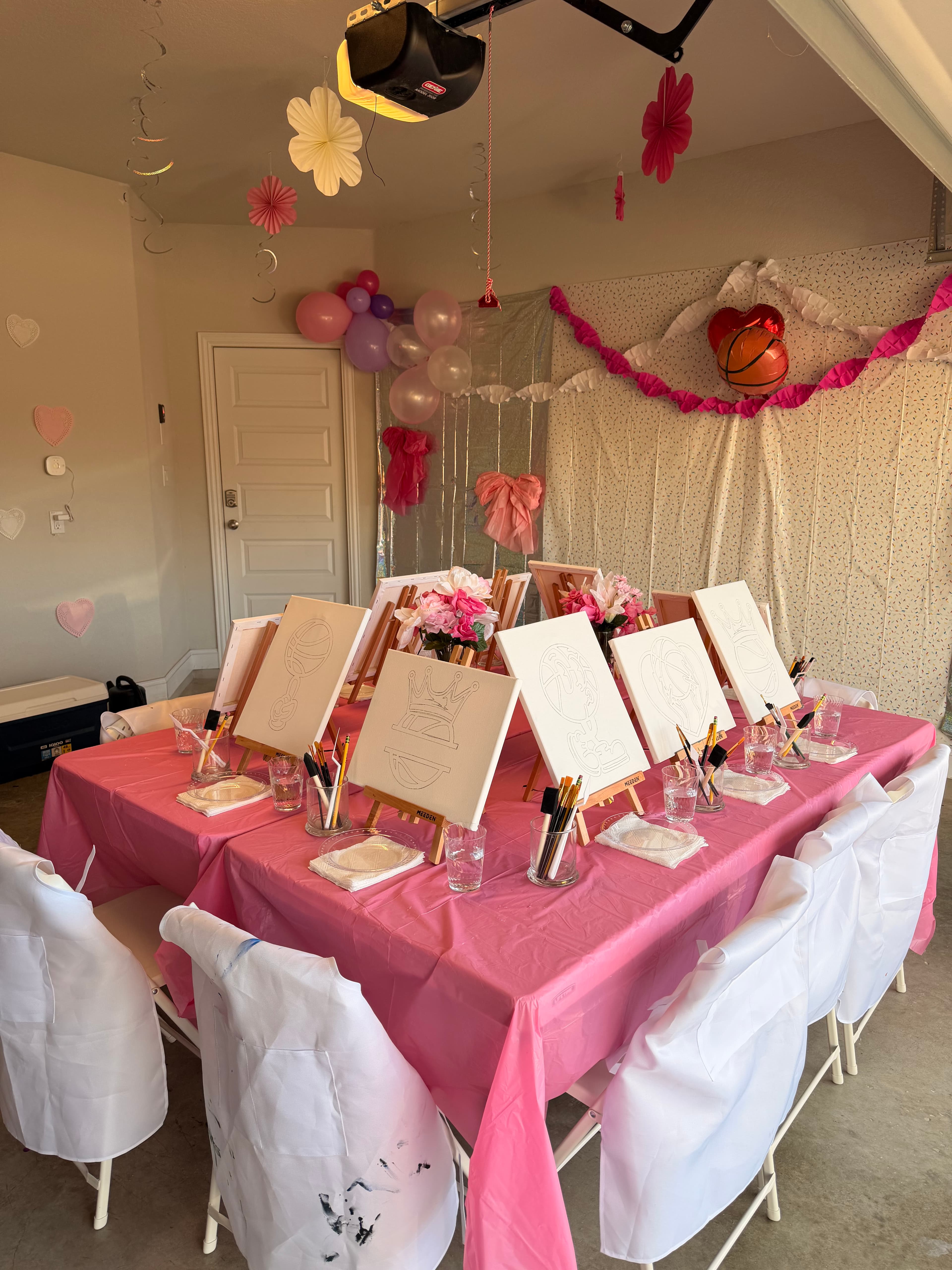 An image of a table with a pink tablecloth. On the table are canvas' with designs on them, ready to be painted