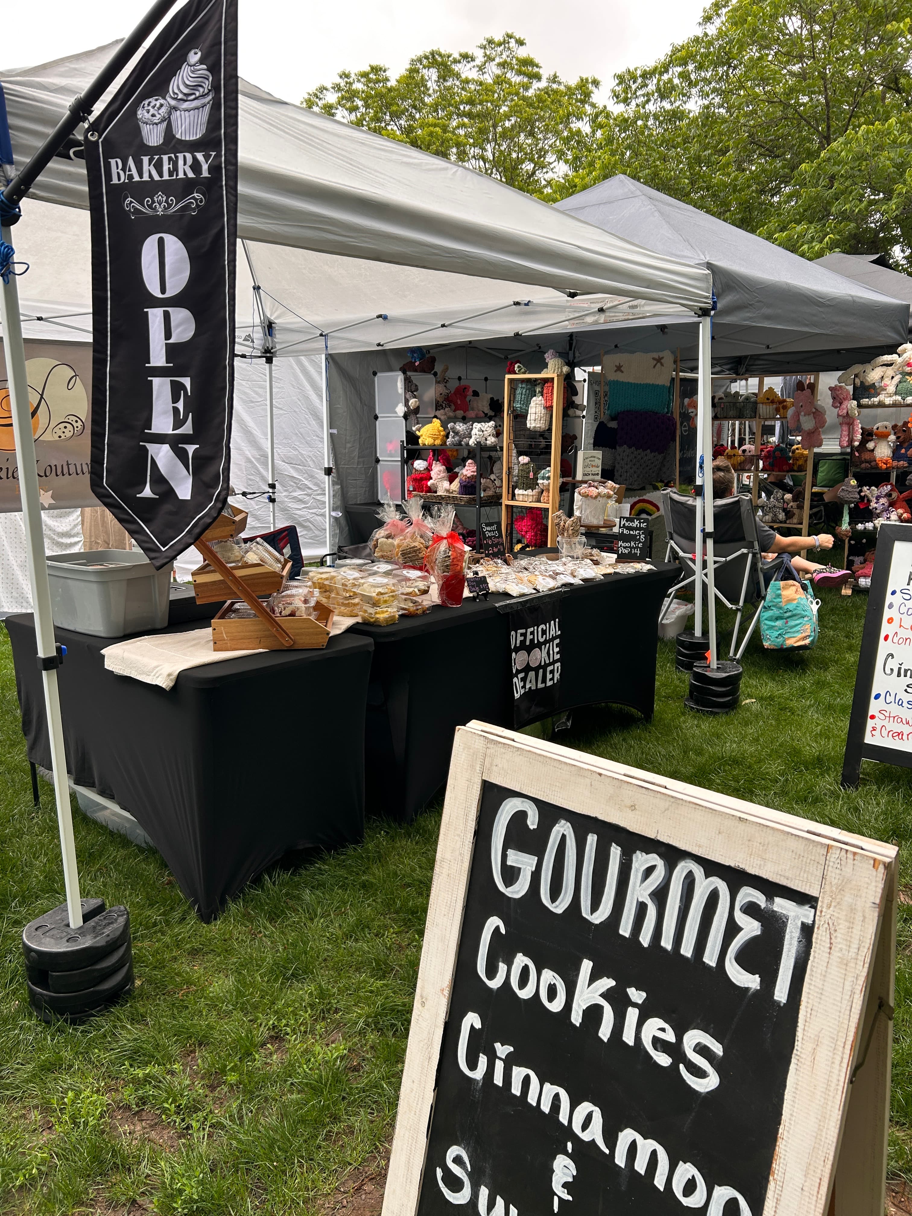 An image of Kookie Kouture's vendor set up: A black tablecloth with baked goods sitting on top. The tablecloth reads "Official Cookie Dealer"