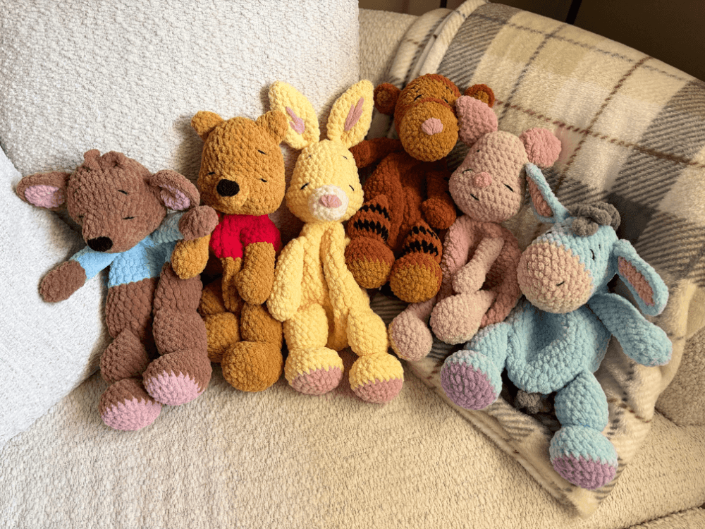 An image of various crocheted kangaroo, bear, rabbit, tiger, piglet and donkey sitting on soft grey blankets